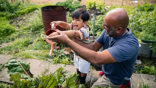 Un uomo aiuta un bambino sorridente ad innaffiare le piante in un giardino