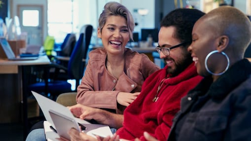 Tre persone sedute in ufficio, guardano documenti e ridono