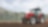 Un trattore rosso che ara un campo fangoso con alberi sullo sfondo