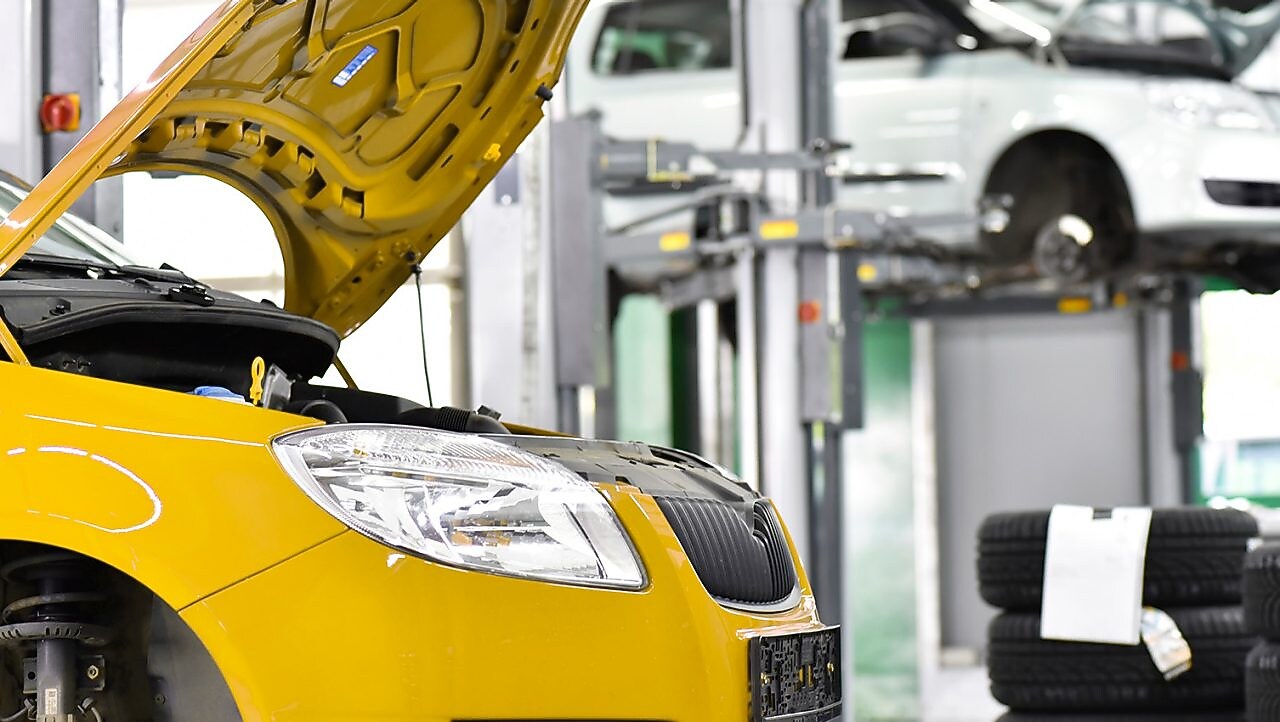 due auto in un garage, una gialla e una bianca, con il cofano aperto e pneumatici sullo sfondo