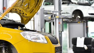 due auto in un garage, una gialla e una bianca, con il cofano aperto e pneumatici sullo sfondo