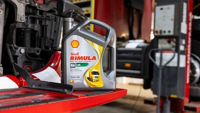 A bottle of Shell Rimula heavy-duty diesel engine oil placed on a red truck part inside a workshop.