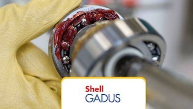 Primo piano macro: un cuscinetto a sfere immerso in un grasso al litio giallo trasparente, isolato su sfondo bianco con spazio per il testo — concetto ingegneristico e industriale.