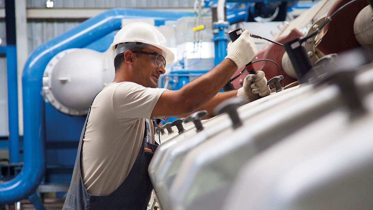 Tecnico che esegue manutenzione su un motore a gas stazionario in un impianto di produzione energetica.
