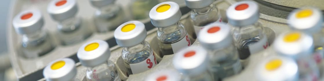 Fiale di medicine in fila posate su un contenitore, alcune con punti rossi sul coperchio, altre con punti gialli sul coperchio