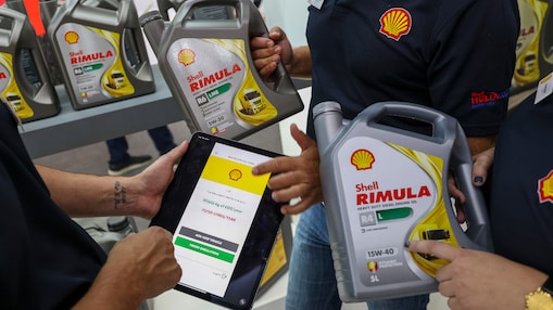 Tre persone con in mano le lattine Shell Rimula e un tablet con l'esposizione di Shell CO2 ed Energy Tracker. Lo sfondo mostra scaffali con altre lattine di Shell Rimula.