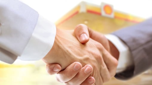 Two businessmen shake your hands with a Shell station in the background