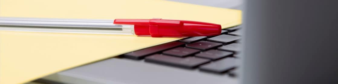 Red pen and yellow sheet of paper on the keyboard of a laptop