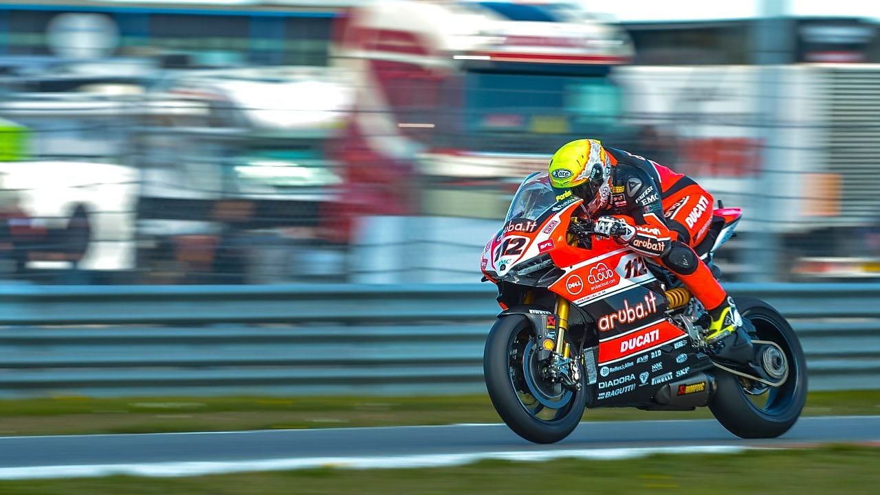 Ducati superbike with rider racing on a track with lorries in the background