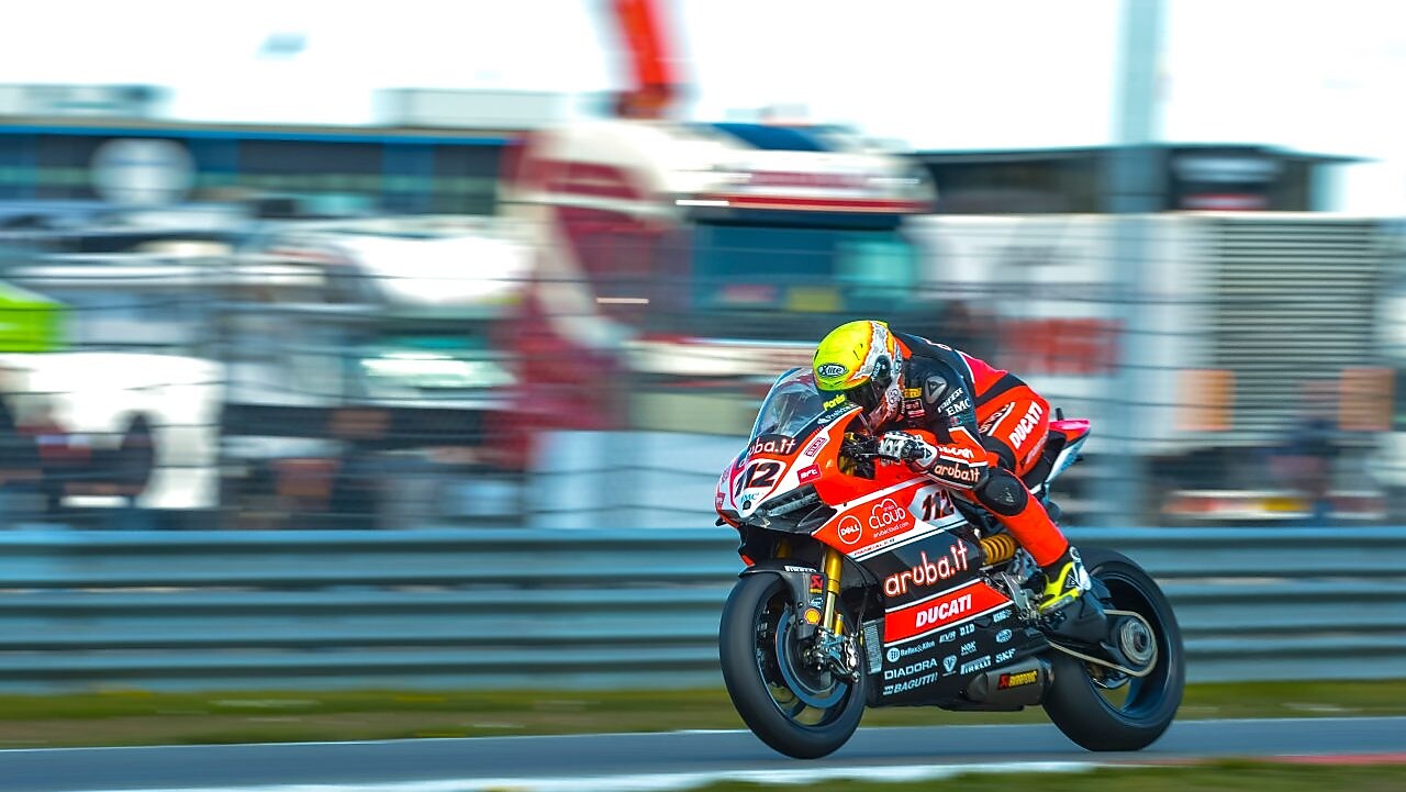 Ducati superbike with rider racing on a track with lorries in the background