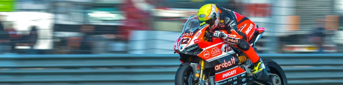 Ducati superbike with rider racing on a track with lorries in the background