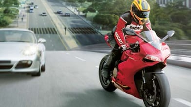 Moto rossa e pilota su una strada con auto ed edifici sullo sfondo