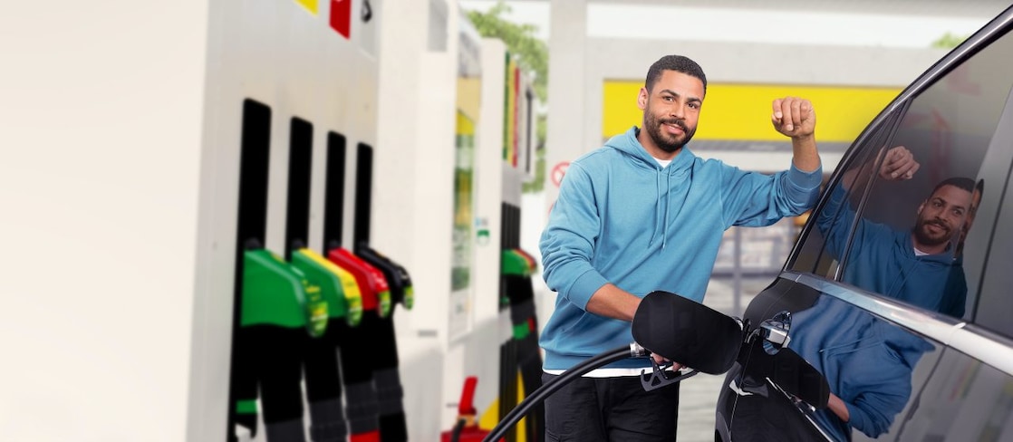 Young man stands at his car and fills up