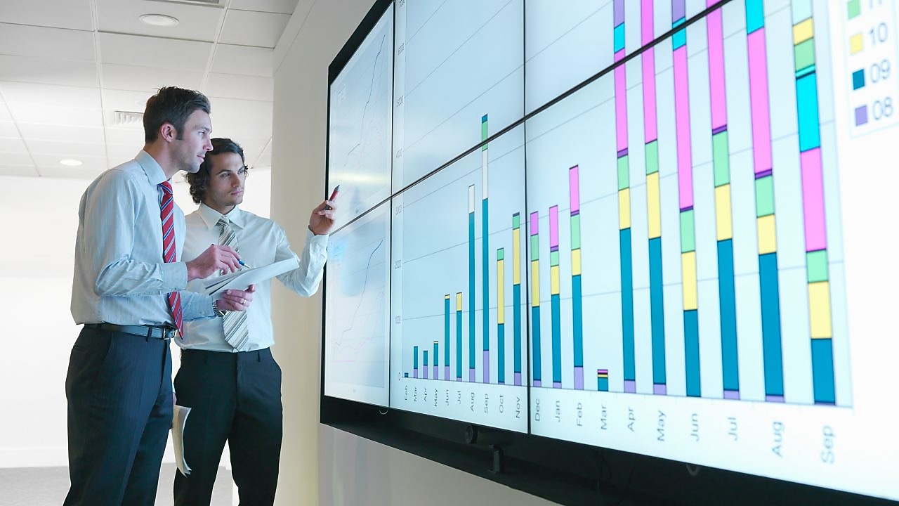 Uomini d'affari analizzano i rapporti visualizzati su un grande schermo digitale