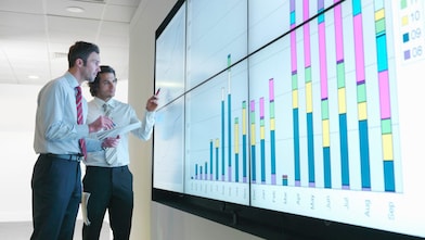 Uomini d'affari analizzano i rapporti visualizzati su un grande schermo digitale